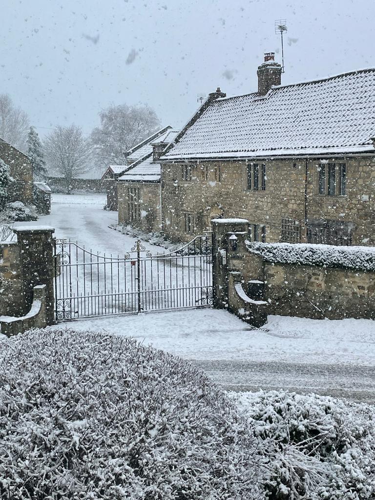 The Old Manor House of Farnham under heavy snowfall, with iron gates and snow-laden hedges in the foreground