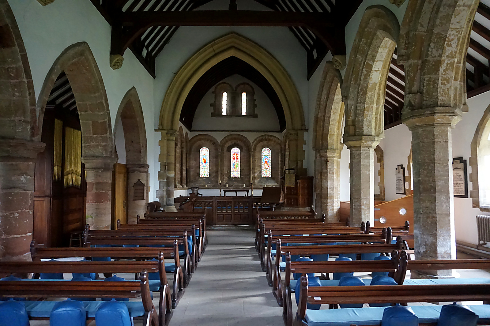 The nave of St Oswald's looking east towards the chancel arch, with stone columns and pews