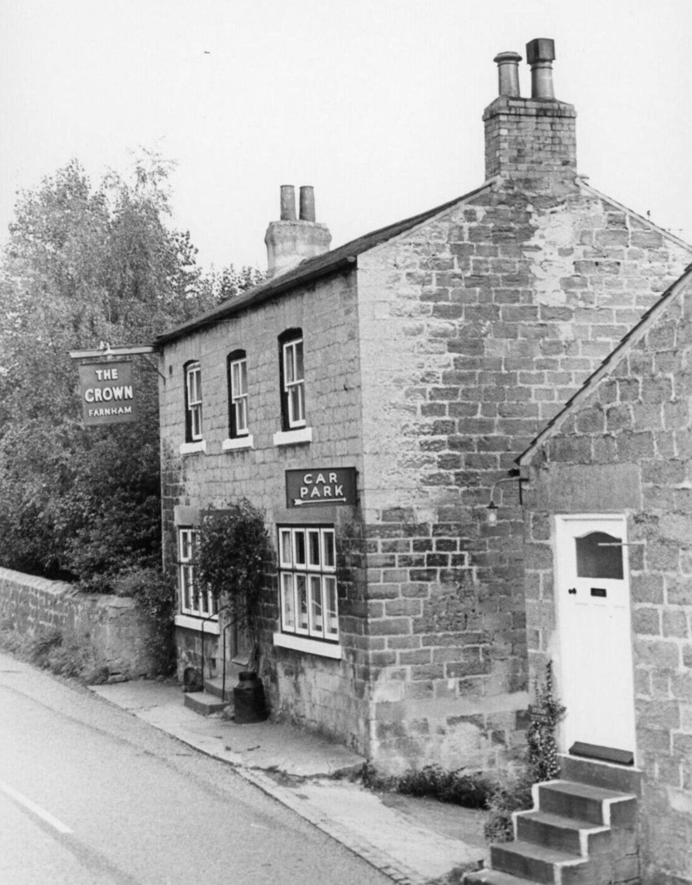 Original black-and-white photograph of the Crown Inn, Farnham, c. 1972, seen from the side. Twin chimneys, the 'The Crown Farnham' hanging sign, and a 'Car Park' arrow sign on the gable end.