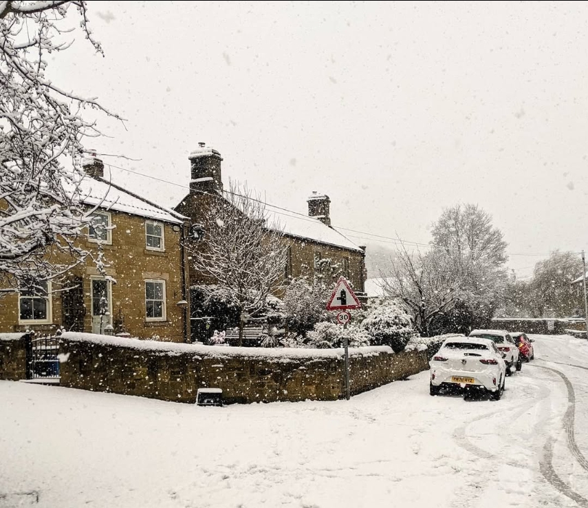 A stone-built Farnham village house with three chimneys, photographed during heavy falling snow, with snow-covered garden walls in the foreground