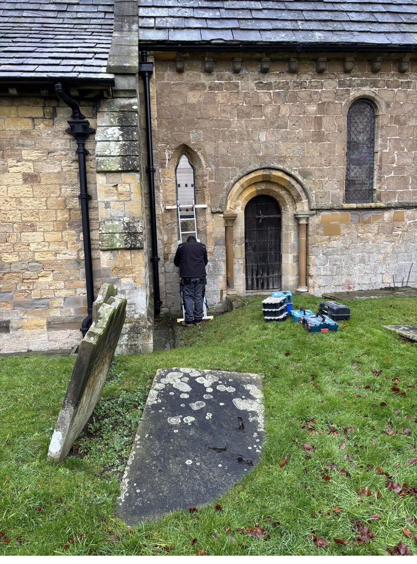 A conservator working at the exterior of St Oswald's Church, Farnham, beside the chancel window during the restoration