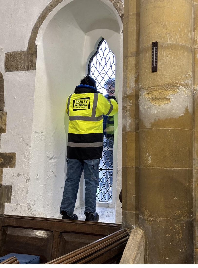 A conservator from Barley Studio in a high-visibility jacket working at the window inside St Oswald's during the installation of the protective glazing